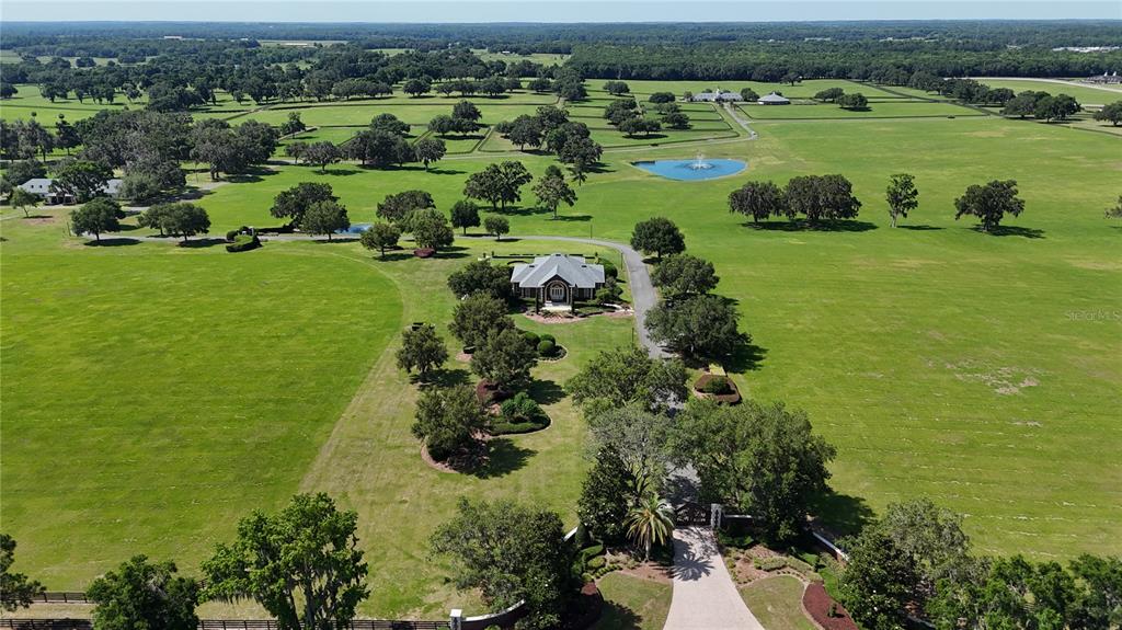 An aerial view shows a brick house with a gray roof surrounded by expansive green pastures — 6800 SE 193RD STREET, MICANOPY, FL