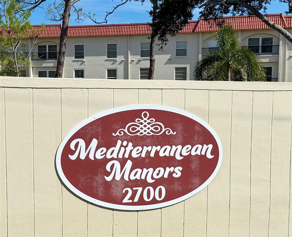 A multi-story apartment building with a red tile roof and a red car parked nearby — 2700 BAYSHORE BOULEVARD UNIT 2108, DUNEDIN, FL