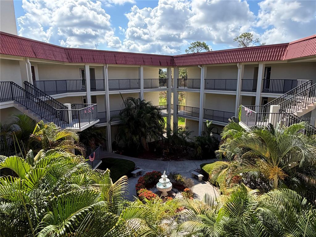 An elevated view of a multi-story apartment courtyard featuring a central fountain and palm trees — 2700 BAYSHORE BOULEVARD UNIT 2108, DUNEDIN, FL