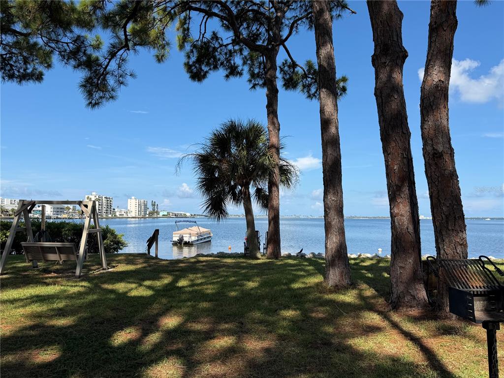 A grassy waterfront yard features a swing set, a grill, and a boat on the water — 2700 BAYSHORE BOULEVARD UNIT 2108, DUNEDIN, FL