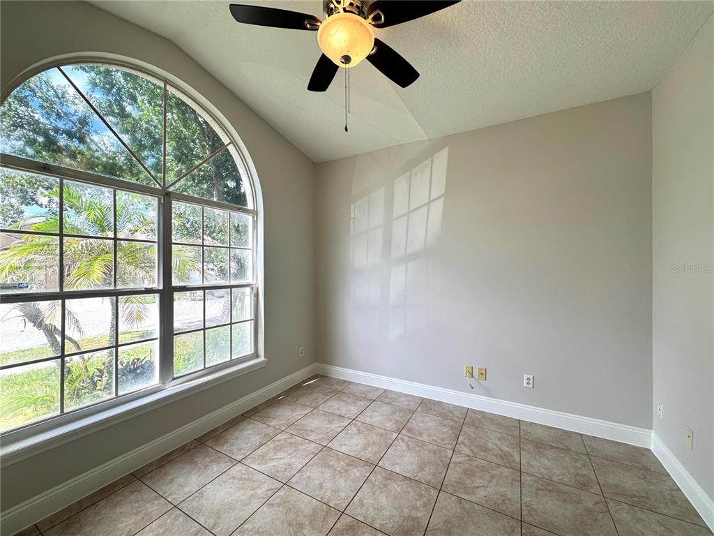 An empty room features beige walls, tile flooring, a ceiling fan, and a large arched window — 11273 MOONSHINE CREEK CIRCLE, ORLANDO, FL