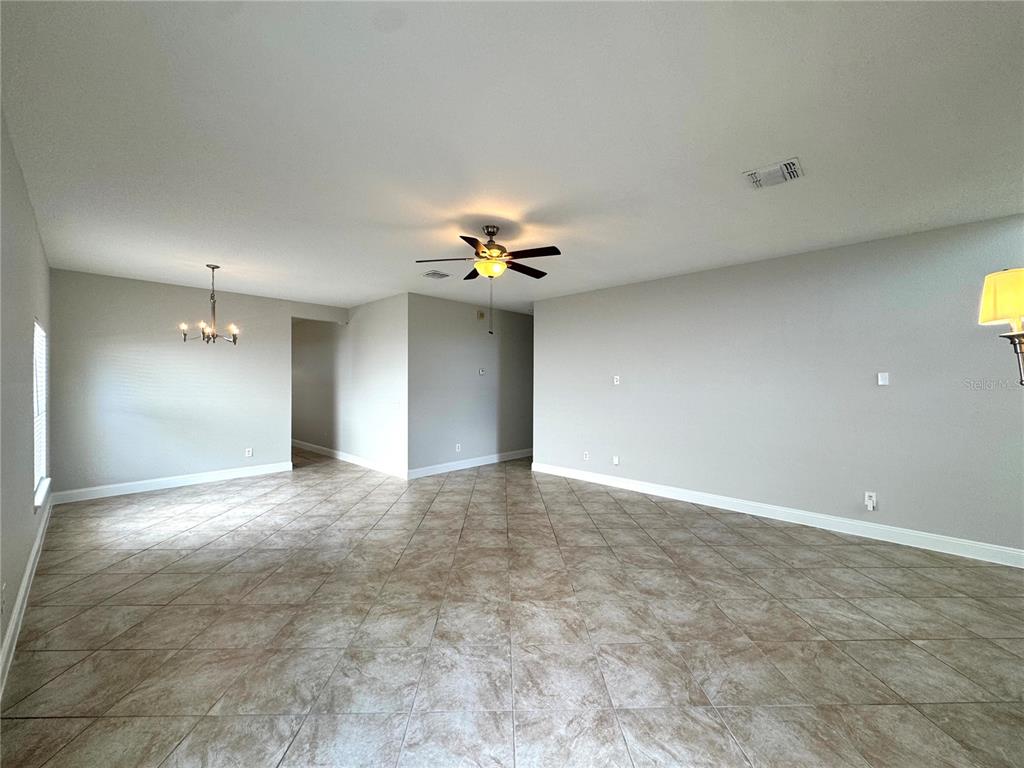A spacious, open-concept living area features light-colored tile flooring, neutral walls, and a ceiling fan — 11273 MOONSHINE CREEK CIRCLE, ORLANDO, FL