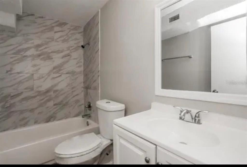A bathroom features a white vanity, a toilet, and a bathtub with marble-patterned tile walls — 918 VALMAR STREET, BRANDON, FL