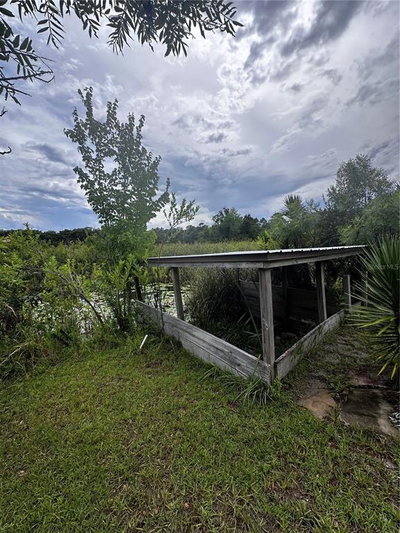 A wooden, open-sided shed structure sits on a grassy lawn next to a pond — 15080 NE 242ND AVENUE, SALT SPRINGS, FL