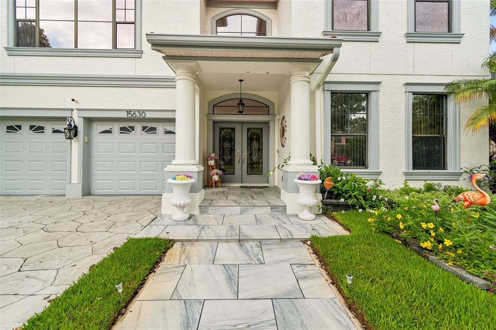 A two-story house exterior features a covered entryway with columns, stone walkway, and garage — 15630 N HIMES AVENUE, TAMPA, FL