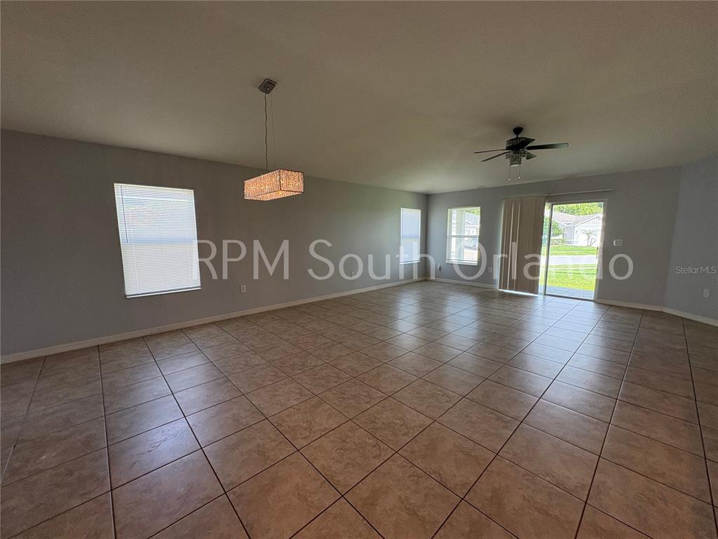 A spacious living room features light-colored tile flooring, a ceiling fan, and a hanging light fixture — 4751 MAPLEWILD LANE, ST CLOUD, FL