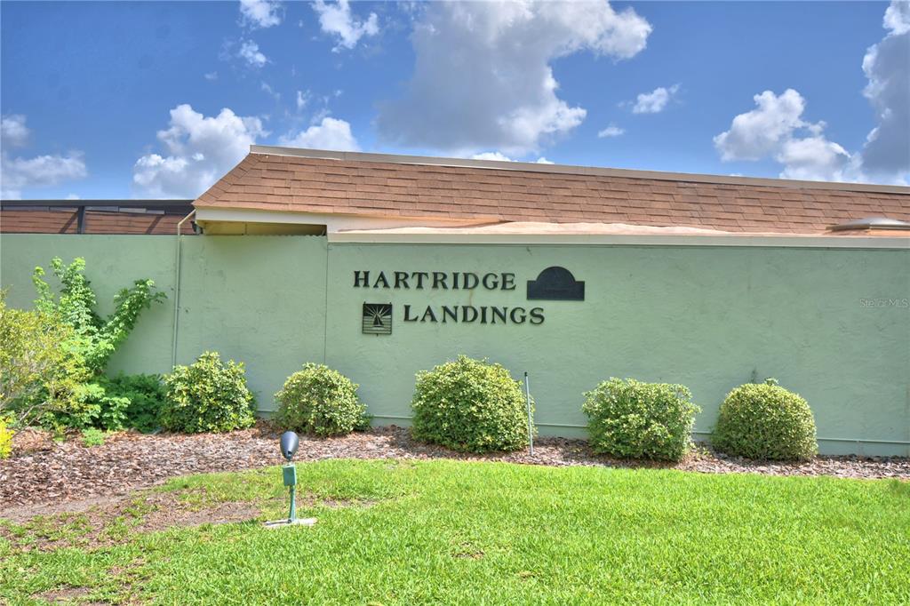 A green wall displays the Hartridge Landings sign above a row of bushes and grass — 2216 STARBOARD, WINTER HAVEN, FL