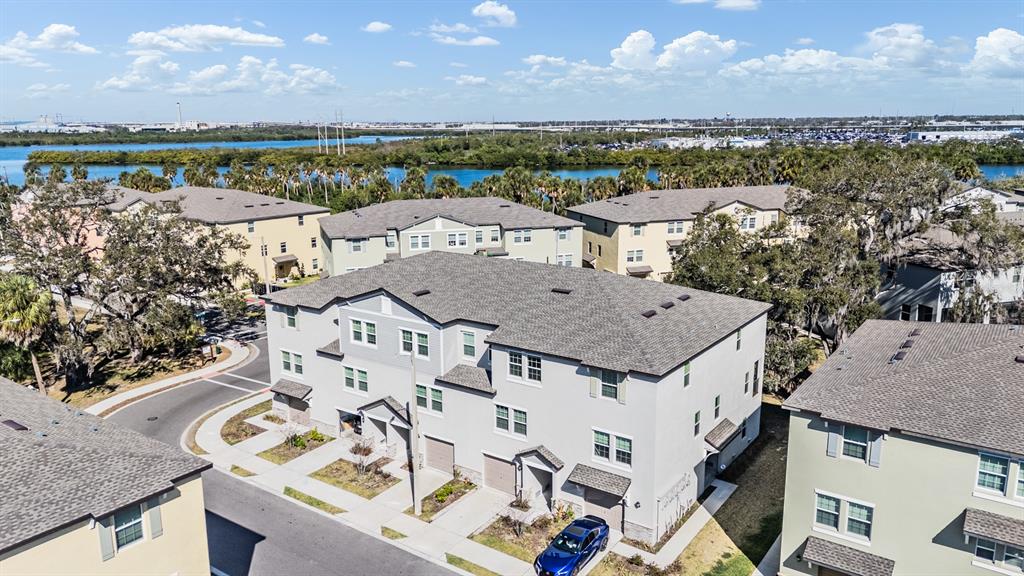 An aerial view shows multi-story townhomes with gray roofs and light-colored siding near a lake — 4607 TUSCAN LOON DRIVE, TAMPA, FL
