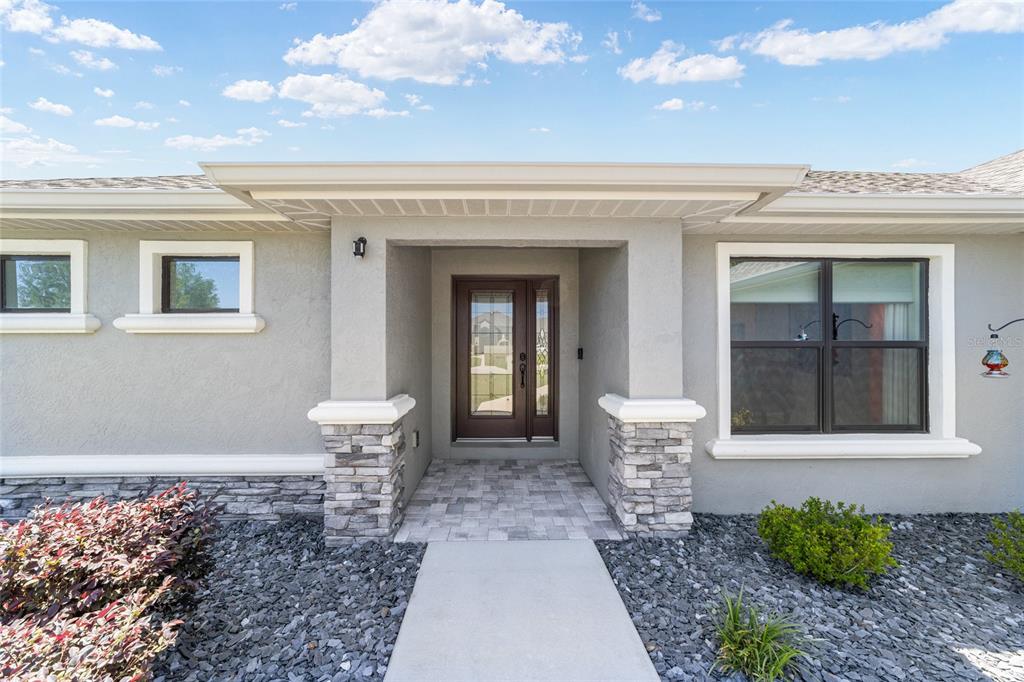 The exterior of a house features a stone-accented entryway, a glass-paneled door, and gray stucco walls — 38 S POLESTAR POINT, INVERNESS, FL