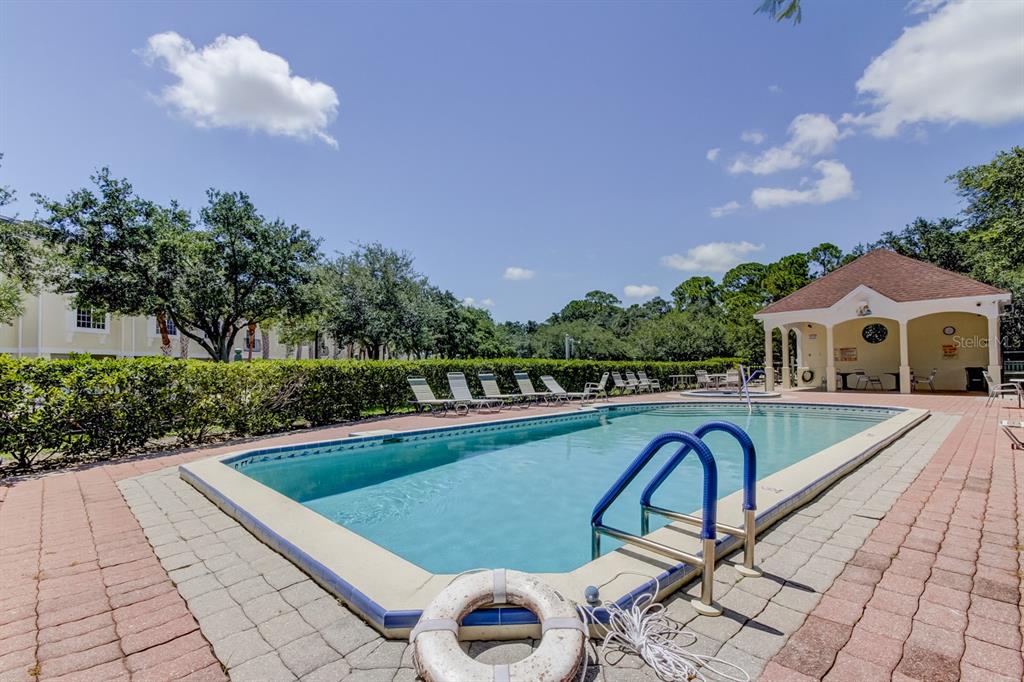 An outdoor swimming pool with a life ring and a covered pavilion under a blue sky — 129 BRENT CIRCLE, OLDSMAR, FL