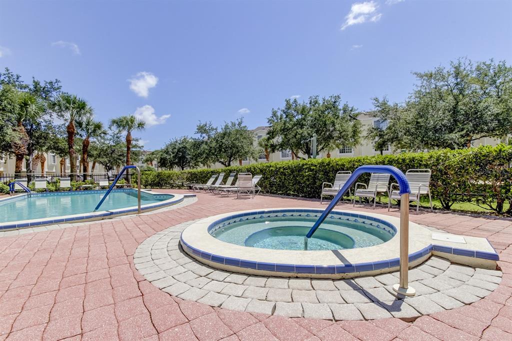 A swimming pool and a circular hot tub are surrounded by a paved deck and landscaping — 129 BRENT CIRCLE, OLDSMAR, FL