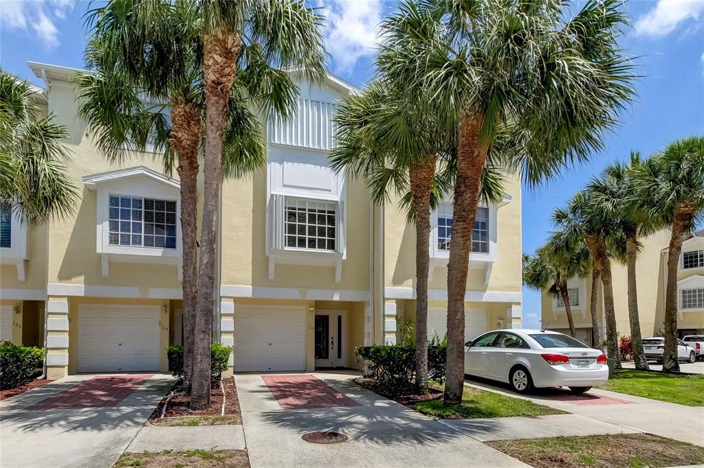 A yellow three-story townhouse with palm trees, a white car, and two garage doors — 129 BRENT CIRCLE, OLDSMAR, FL