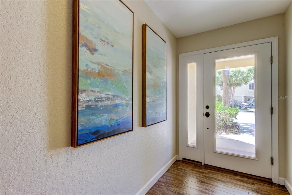 An entryway features two abstract paintings on a beige wall, wood flooring, and a door — 129 BRENT CIRCLE, OLDSMAR, FL