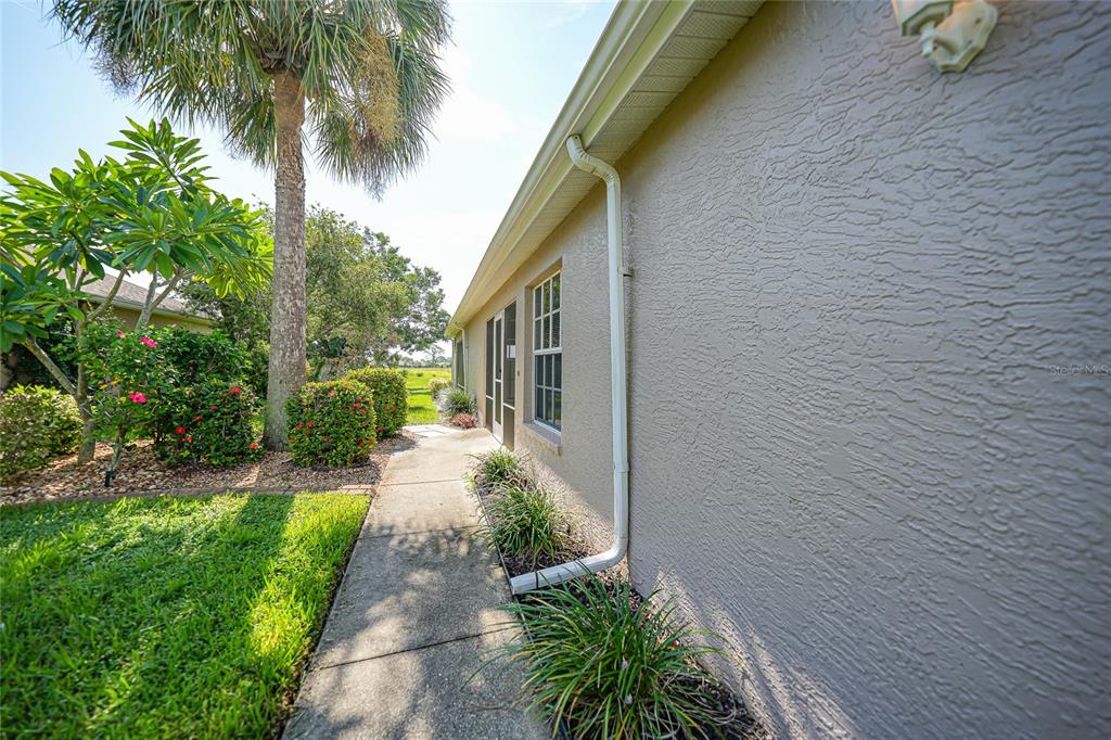 A concrete walkway runs along the side of a house with beige stucco walls — 4214 FAIRWAY PLACE, NORTH PORT, FL
