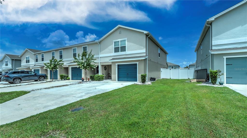 A two-story townhouse exterior features a concrete driveway, a blue garage door, and a small tree — 2933 FIELDWOOD CIRCLE, ST CLOUD, FL