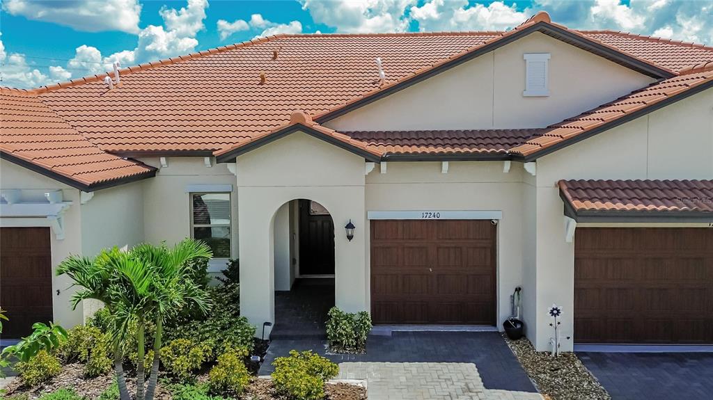 An exterior view of a house with a tiled roof, arched entryway, and two garages — 17240 HOLLY WELL AVENUE, WIMAUMA, FL