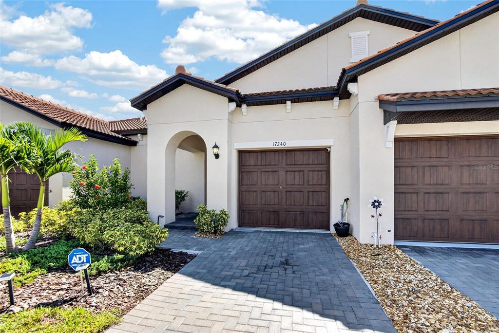 A beige house exterior features a brown garage door, a paved driveway, and landscaping — 17240 HOLLY WELL AVENUE, WIMAUMA, FL
