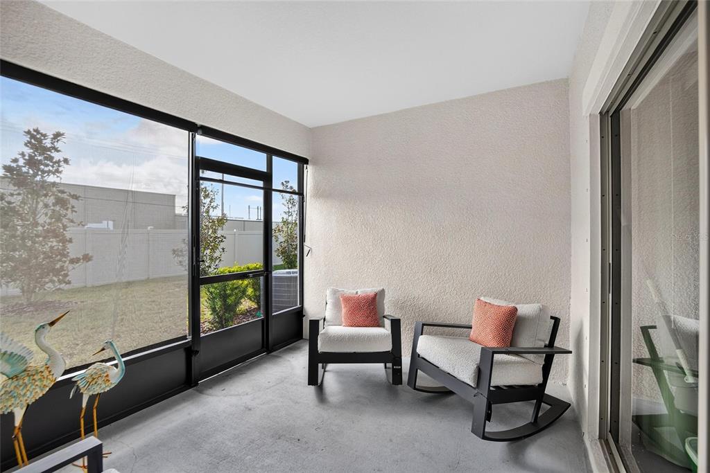 A screened-in patio features two rocking chairs, a concrete floor, and a view of a yard — 17240 HOLLY WELL AVENUE, WIMAUMA, FL
