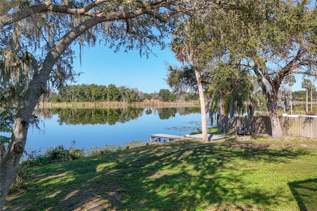 A grassy backyard slopes down toward a lake with a wooden dock and mature trees — 264 S CENTRAL AVENUE, UMATILLA, FL