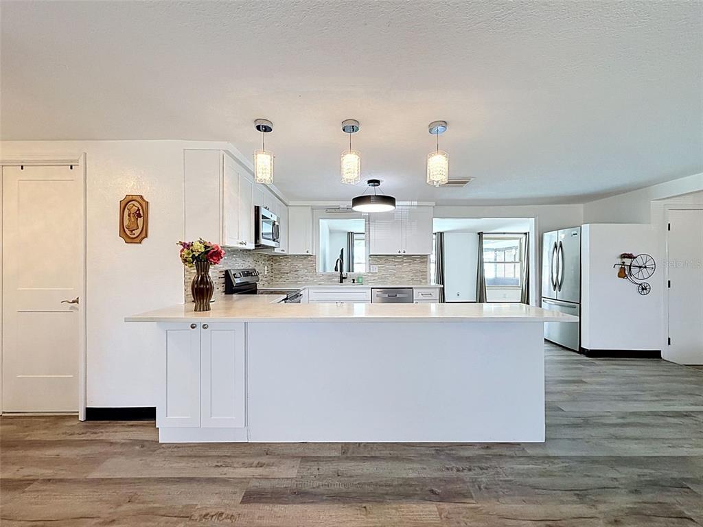A kitchen features a white island, light countertops, stainless steel appliances, and wood-look flooring — 12735 1ST ISLE, HUDSON, FL