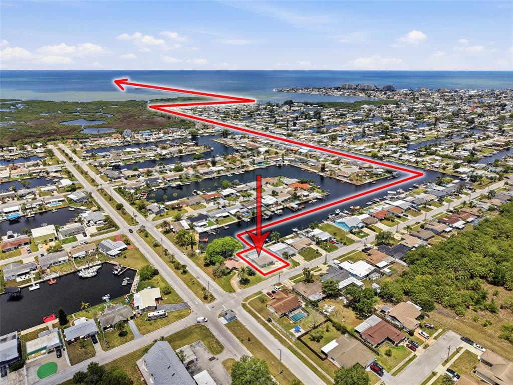 An aerial view shows a residential property with a pool near a canal and bay — 12735 1ST ISLE, HUDSON, FL