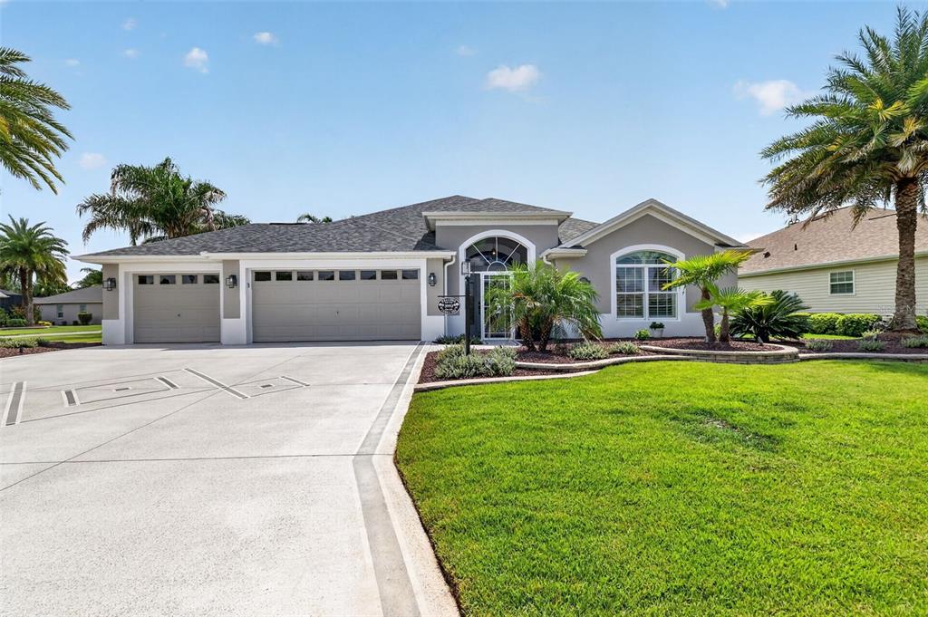 A single-story house with a three-car garage, gray exterior, and a landscaped front lawn — 3992 NEIGHBORLY WAY, THE VILLAGES, FL