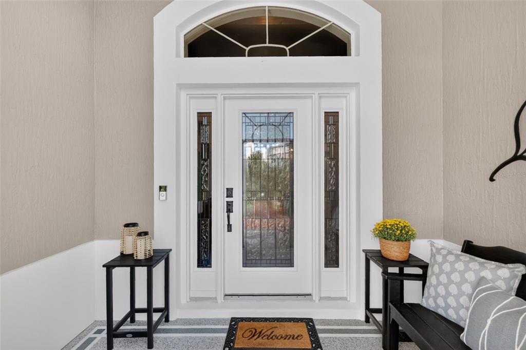 A white front door with glass panels and a transom window sits on a covered porch — 3992 NEIGHBORLY WAY, THE VILLAGES, FL