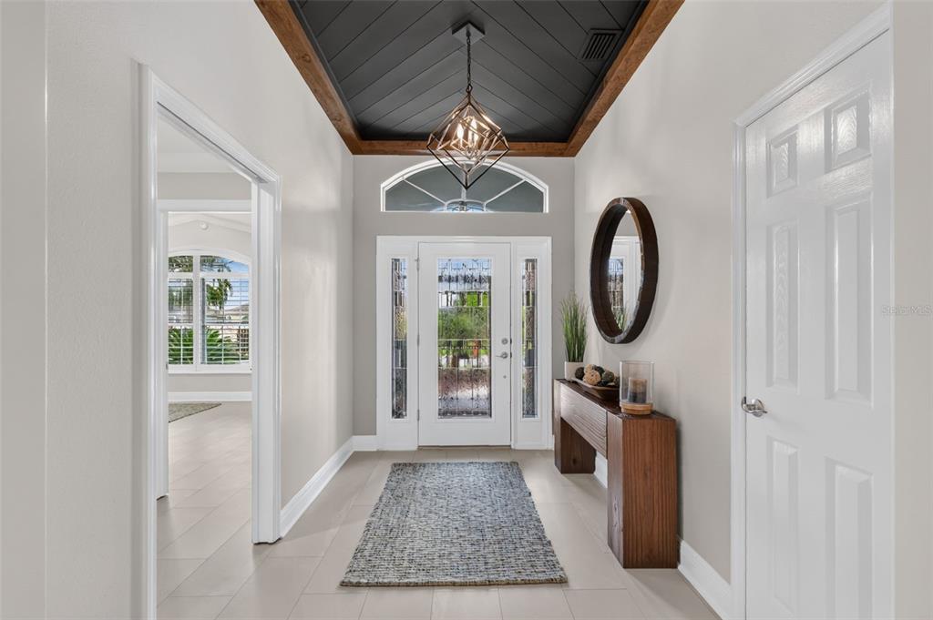 A bright entryway features a dark tray ceiling, a geometric chandelier, and a wooden console table — 3992 NEIGHBORLY WAY, THE VILLAGES, FL