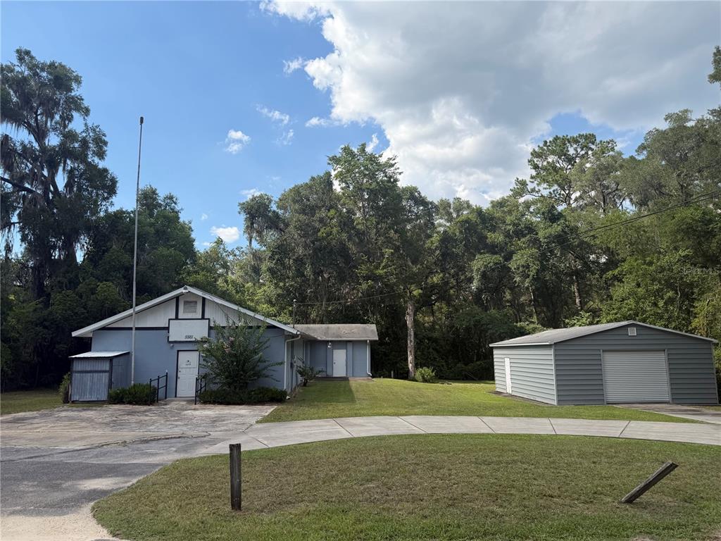 A blue building with a detached metal garage sits on a grassy lot with trees — 5561 NE 35TH STREET, SILVER SPRINGS, FL