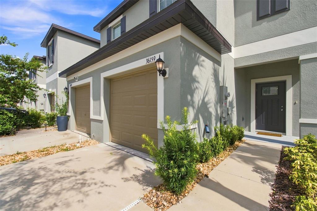 A two-story townhouse exterior with a tan garage door, gray stucco walls, and front entrance — 36159 RISA MICHELE STREET, ZEPHYRHILLS, FL