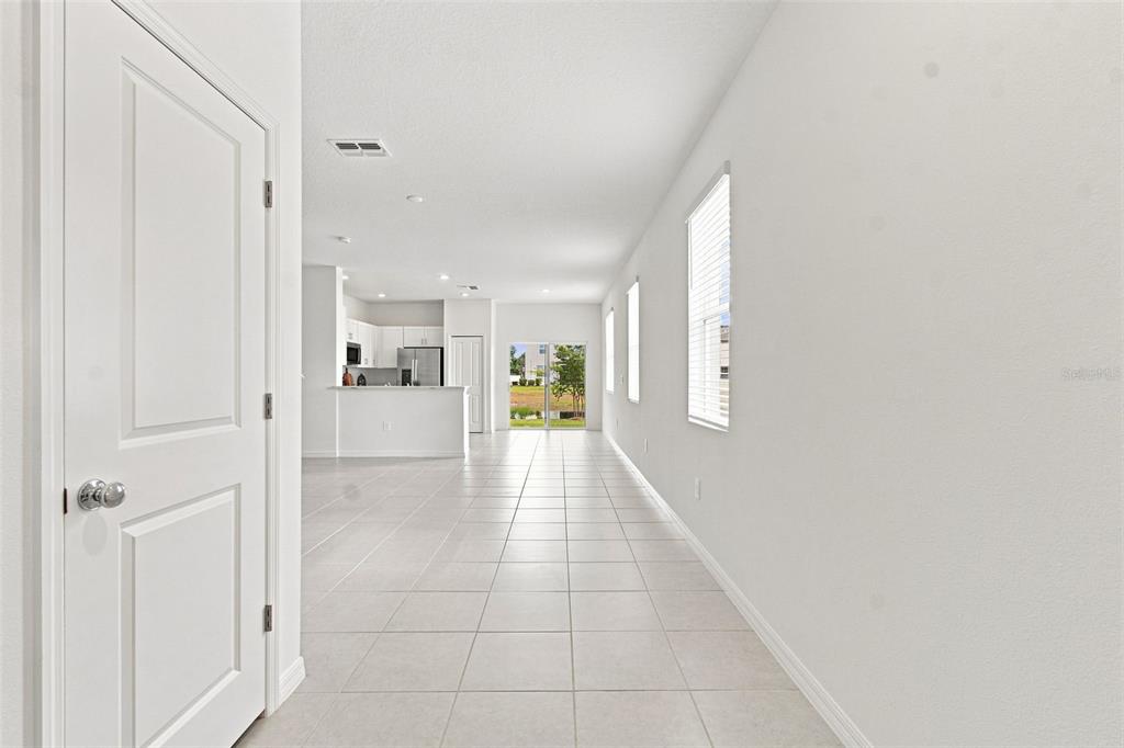 A bright, open-concept living area with white tile flooring leads to a kitchen and patio — 36159 RISA MICHELE STREET, ZEPHYRHILLS, FL