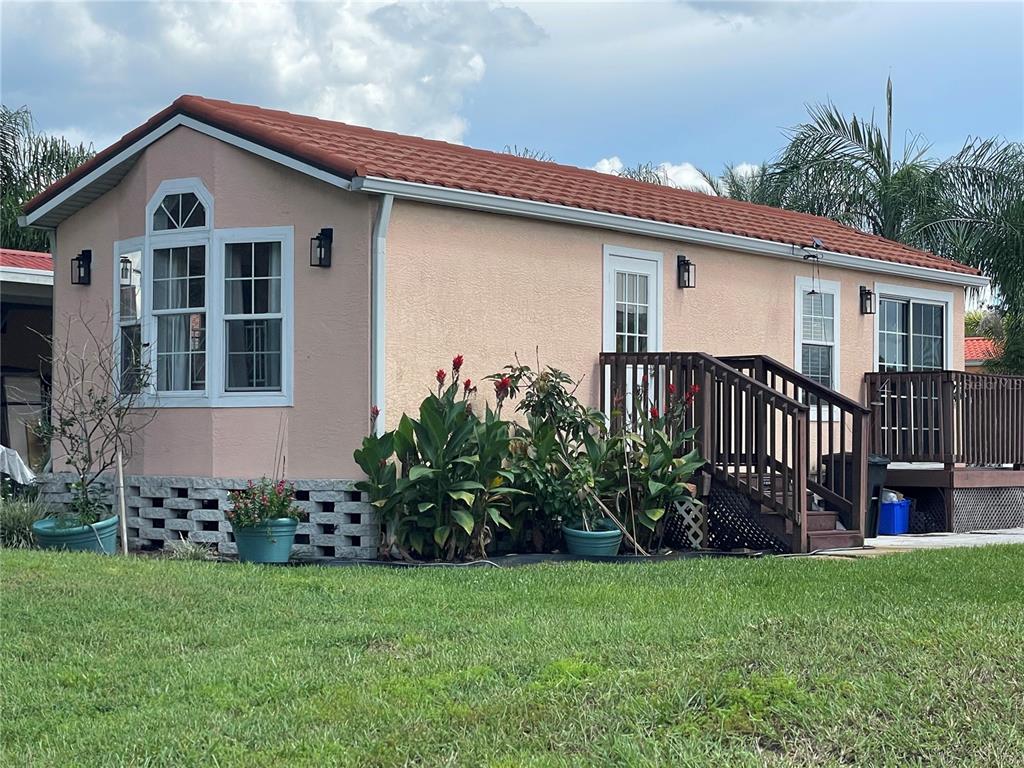 A peach-colored mobile home with a red tile roof, wooden deck, and landscaping — 21127 SAN PABLO DRIVE, LAND O LAKES, FL