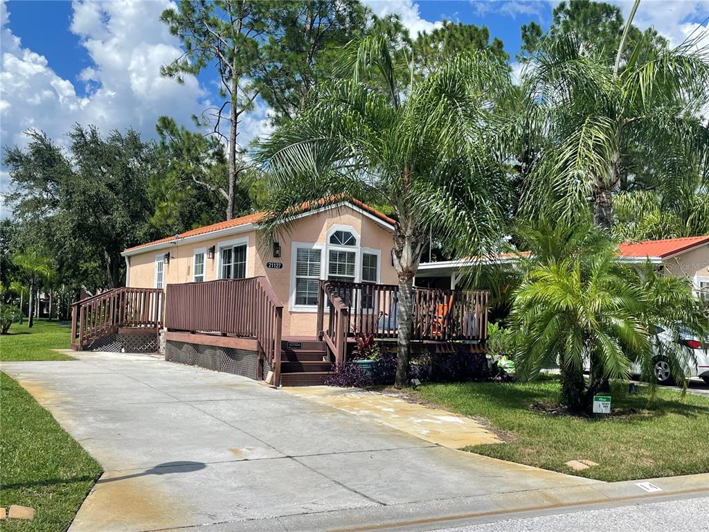 A peach-colored mobile home features a wooden deck, a concrete driveway, and surrounding palm trees — 21127 SAN PABLO DRIVE, LAND O LAKES, FL