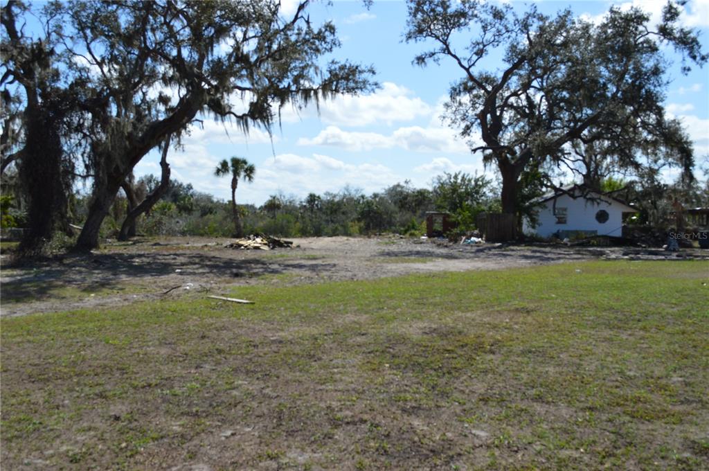 A large, cleared lot features scattered debris, mature oak trees, and a small white building — 7023 PAYNE AVENUE, GIBSONTON, FL