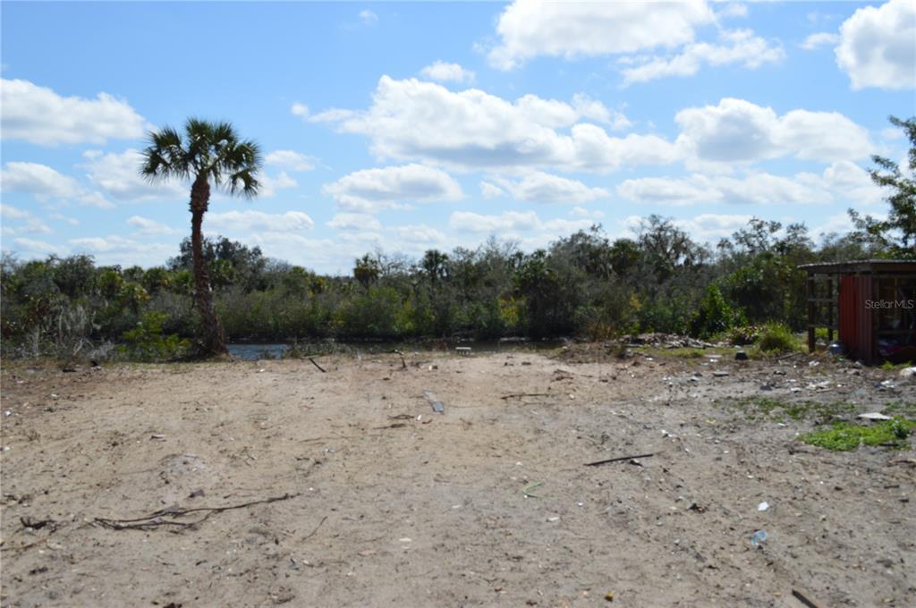 A sandy, undeveloped lot features a single palm tree and a small shed near water — 7023 PAYNE AVENUE, GIBSONTON, FL