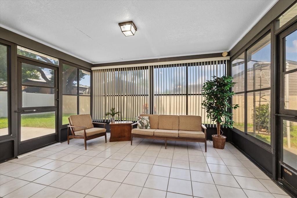 A sunroom with tiled floors, a sofa, an armchair, and large screened windows — 7329 FAIRWOOD AVENUE, NEW PORT RICHEY, FL