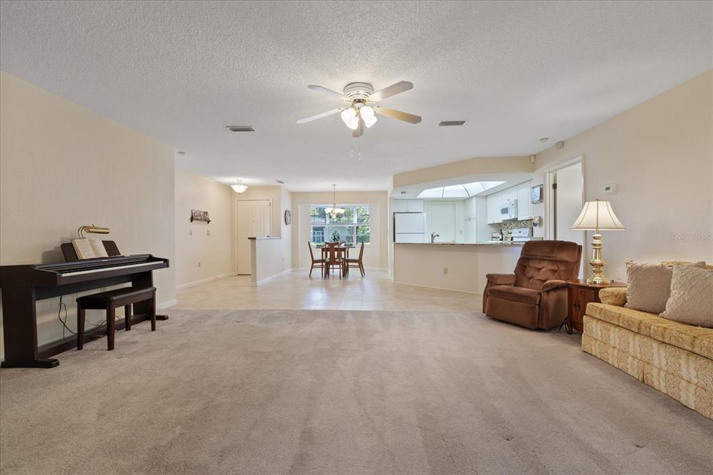 A living room with carpeted flooring transitions into a tiled dining area and kitchen — 7329 FAIRWOOD AVENUE, NEW PORT RICHEY, FL