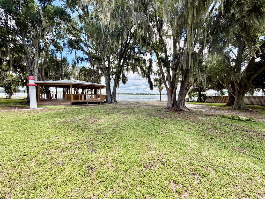 A grassy yard features a wooden gazebo and a decorative lighthouse near a lake — 1702 1/2 US HIGHWAY 92 W, AUBURNDALE, FL