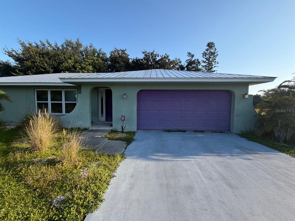 A single-story house features a light green exterior, a purple garage door, and a metal roof — 30168 ALDER ROAD, PUNTA GORDA, FL