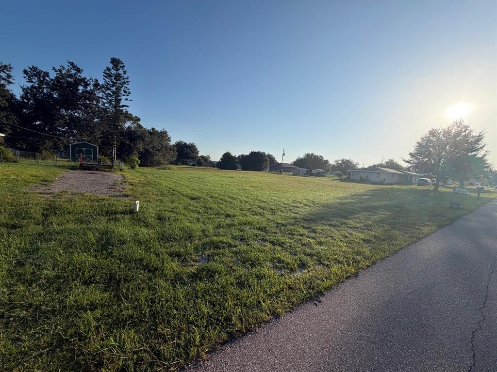 A vacant, grassy lot sits beside a paved road with a small shed in the distance — 30168 ALDER ROAD, PUNTA GORDA, FL