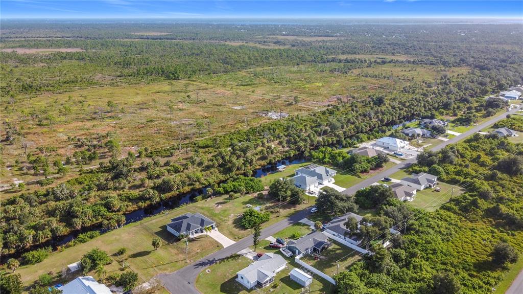 An aerial view shows a suburban street with houses bordering a canal and open land — 11024 EULER AVENUE, ENGLEWOOD, FL