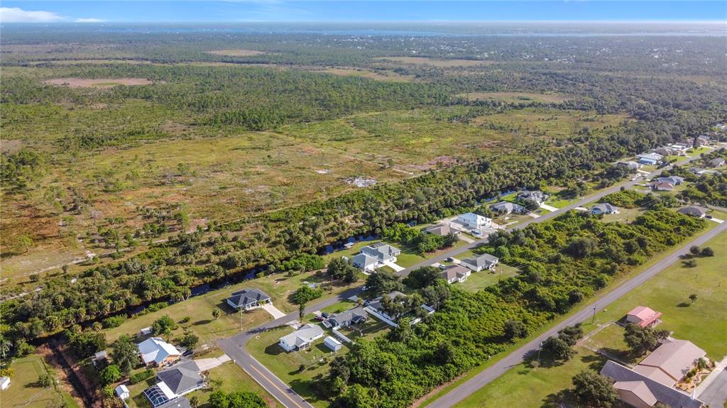 An aerial view shows a residential street with houses bordering a large, undeveloped grassy field — 11024 EULER AVENUE, ENGLEWOOD, FL