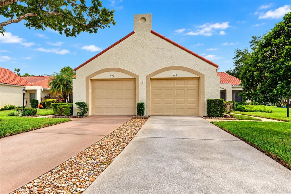 A duplex house exterior features two beige garage doors, a pebble driveway, and a tiled roof — 978 MADRID DRIVE, PALM HARBOR, FL