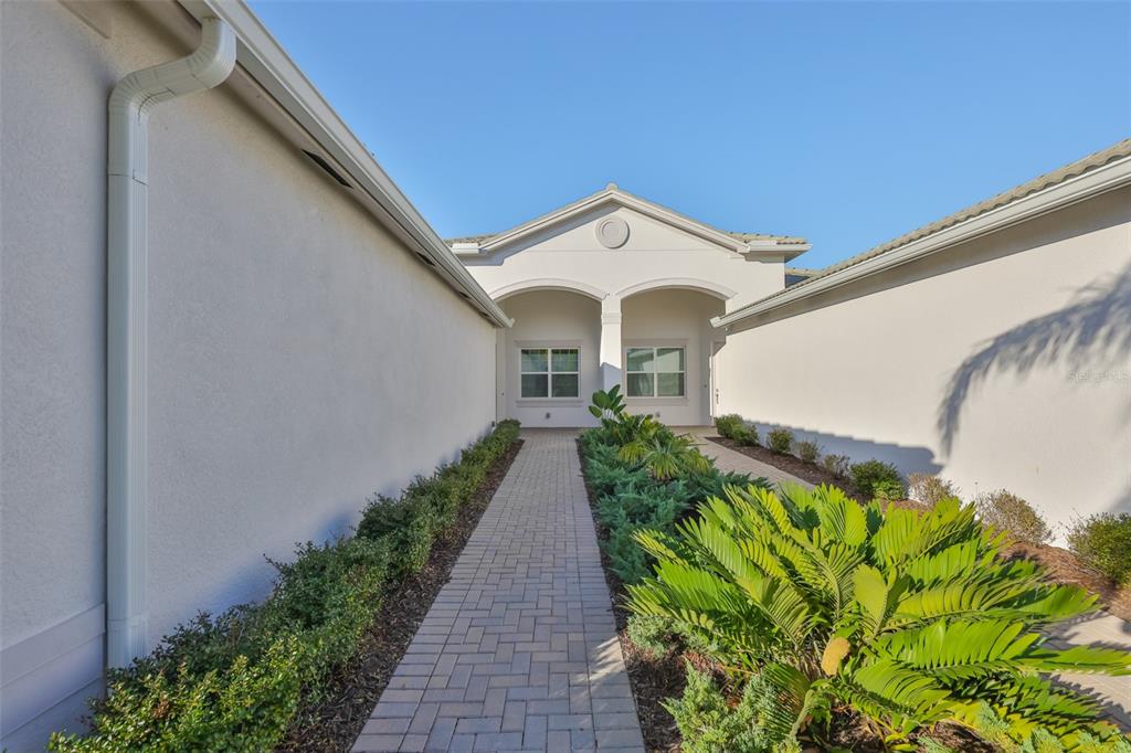 A paved walkway leads to the recessed entryway of a light-colored stucco home — 4906 AVILA LAKES DRIVE, WIMAUMA, FL