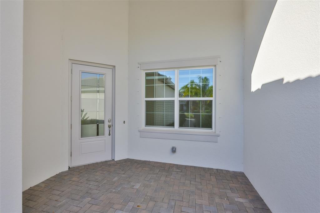 A covered entryway features a white door, a window with muntins, and brick paver flooring — 4906 AVILA LAKES DRIVE, WIMAUMA, FL