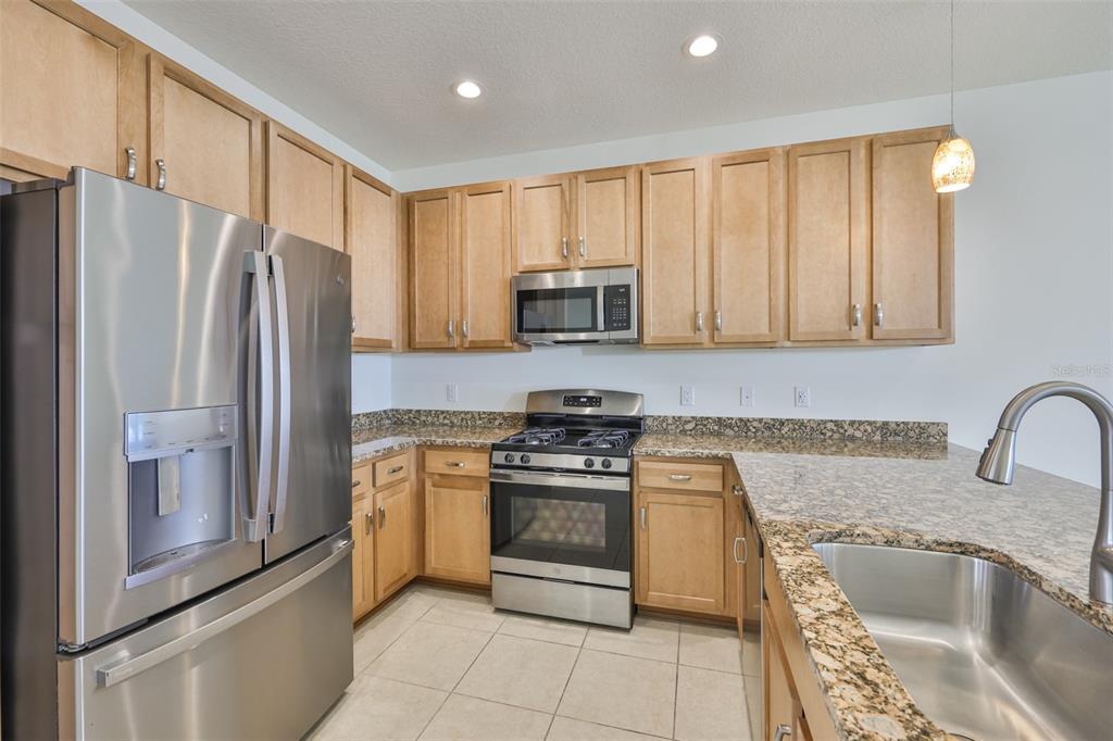 A kitchen features light wood cabinets, granite countertops, stainless steel appliances, and tile flooring — 4906 AVILA LAKES DRIVE, WIMAUMA, FL