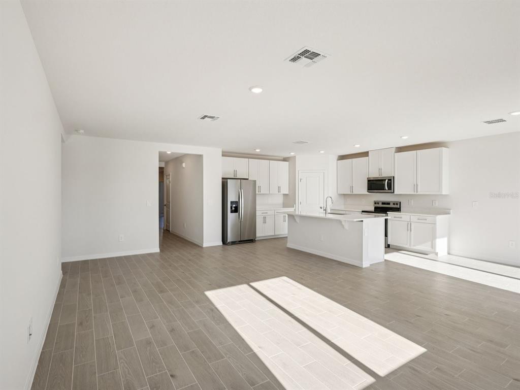 An open-concept kitchen and living area with white cabinets, stainless appliances, and gray tile flooring — 10433 ABUNDANCE GROVE WAY, PARRISH, FL