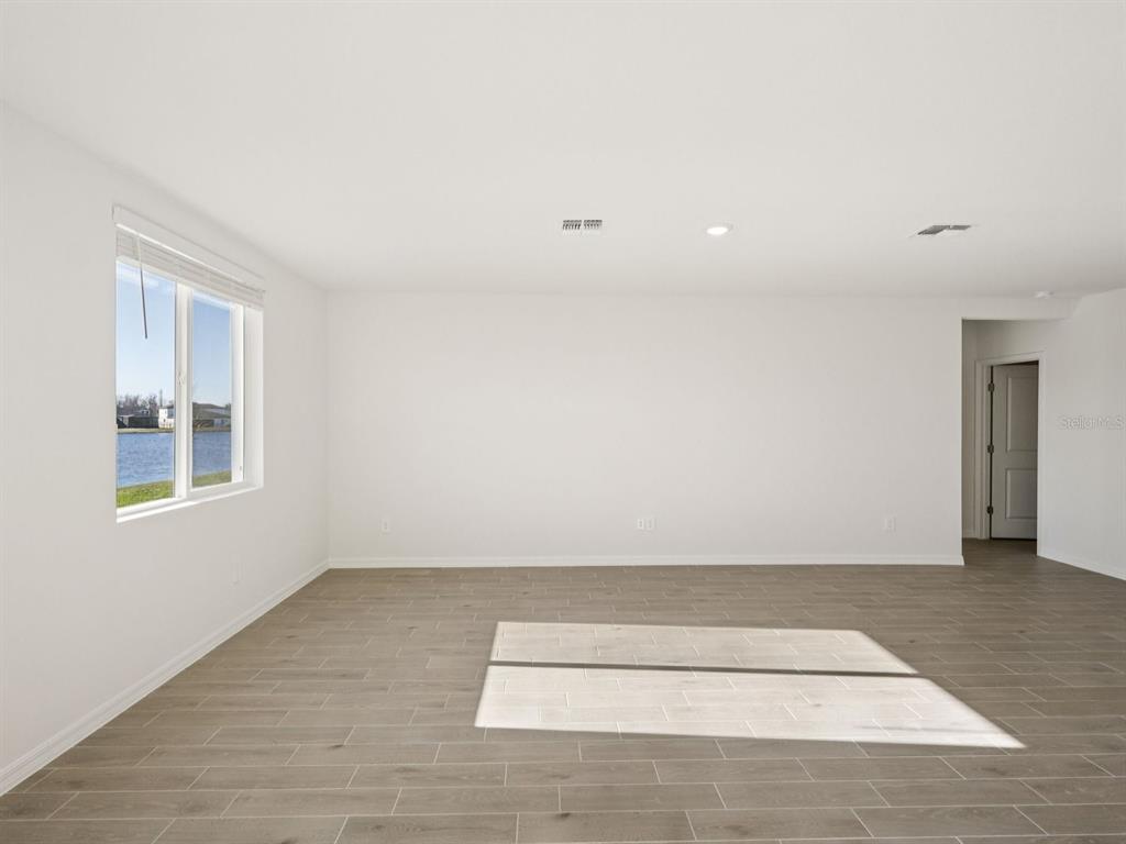 An empty room with light wood-look tile flooring, white walls, and a window overlooking water — 10433 ABUNDANCE GROVE WAY, PARRISH, FL
