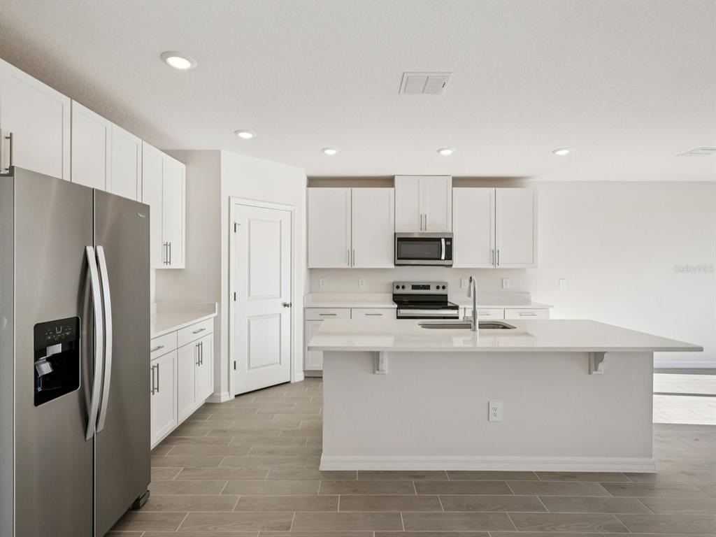 A modern kitchen features white cabinets, stainless steel appliances, a center island, and tile flooring — 10433 ABUNDANCE GROVE WAY, PARRISH, FL
