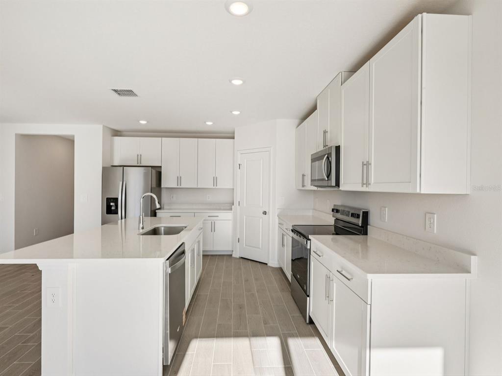 A modern kitchen features white cabinets, quartz countertops, stainless steel appliances, and wood-look tile flooring — 10433 ABUNDANCE GROVE WAY, PARRISH, FL